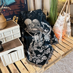 Detail of woven camping blanket showing gothic skull lovers and rose patterns with tassels