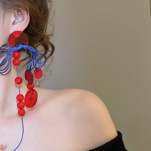 Detail view of long tassel earrings with red resin beads and blue silk thread winding