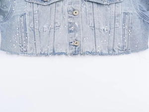 Détails d'une veste en jean bleu clair avec ornements de perles blanches et boutons en métal