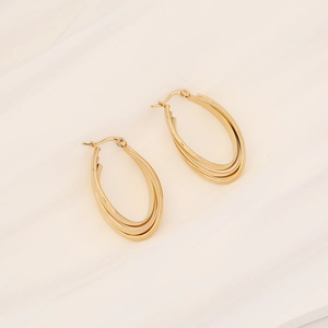 Detailed view of triple-layered oval gold hoop earrings on elegant white satin fabric