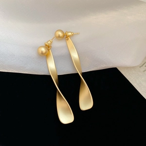 Détail de boucles d'oreilles pendantes géométriques torsadées en or mat avec perles