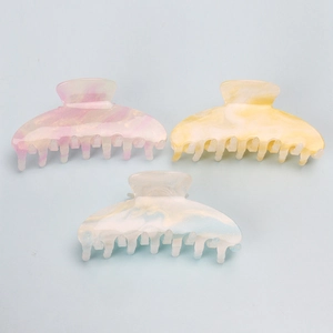 Close-up of three iridescent acrylic hair claws in pink, orange and white marble tones