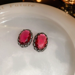 Macro view of vintage oval earrings with red gems in a black gold engraved frame