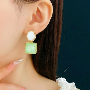Detail einer Frau mit asymmetrischen Ohrringen mit grünen und weißen Geometrie-Elementen