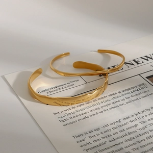 Detail of two gold hammered texture open bangles stacked on a vintage newspaper background