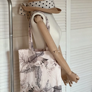 Detail of light pink linen tote bag with black floral patterns on a wooden mannequin