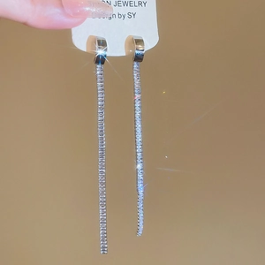 Macro detail of silver tassel earrings with zircon stones on a warm display background