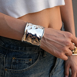 Close-up of a wide polished metallic cuff bracelet with irregular wavy edges and liquid texture