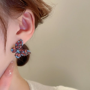 Close-up of model wearing a vintage butterfly stud earring with red and blue zircon