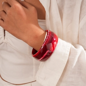 Detail of red marble texture resin bangle on wrist with elegant white apparel
