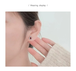 Wearing display of a teardrop-shaped earring with red pear-cut gem and white zircons