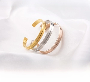 Detail of three stainless steel C-shaped bracelets in gold, silver, and rose gold finishes