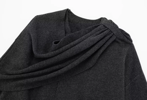 Detailed close-up of dark grey knitted fabric with asymmetric pleated neckline design