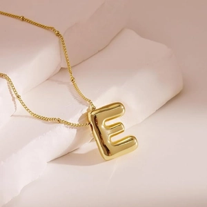 Macro shot of 18K gold plated puffy letter E pendant with bead chain on white stone