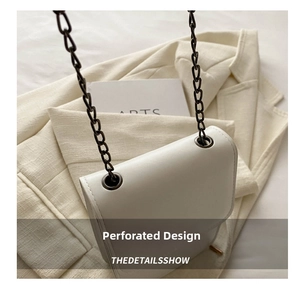 Macro shot of white leather crossbody bag with metal chain strap and eyelet detail