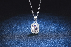 Macro shot of silver emerald-cut moissanite pendant with halo detail on navy blue sand