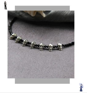Macro shot of gothic black faceted beads and small silver skull charms on a textured fabric