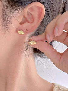 Close-up of golden shell stud earrings with radial texture on a person's ear lobe