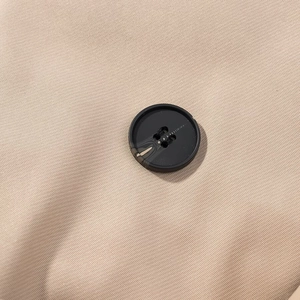 Detail of beige twill fabric texture and black four-hole button on a cropped jacket