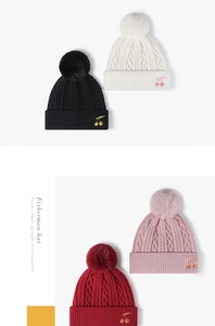 Close-up of thick cable knit winter hat featuring cherry embroidery and soft pom pom