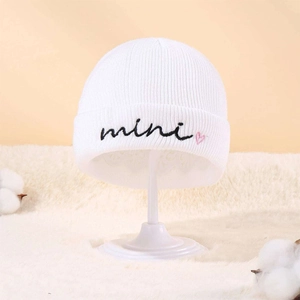 White knit beanie for kids with mini embroidery and pink heart on soft plush background