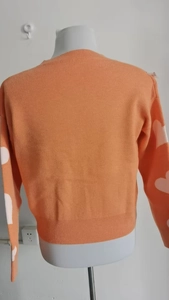 Detail view of orange knit cardigan showing white heart patterns on the long sleeves