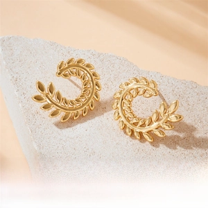Detailed close-up of gold-plated wheat leaf earrings on a minimalist stone texture