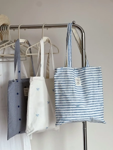 Detailed embroidery of blue bows on striped and gingham canvas tote bags display