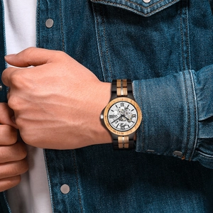 Detail of wooden mechanical watch with hollow gold movement on a denim sleeve