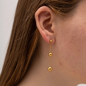 Boucles d'oreilles pendantes en acier doré avec trois perles portées par un mannequin
