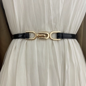 Elegant thin black belt with gold interlocking buckle on a white dress for women