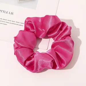 Close-up of a large fuchsia silk scrunchie with a glossy satin texture and dense pleats