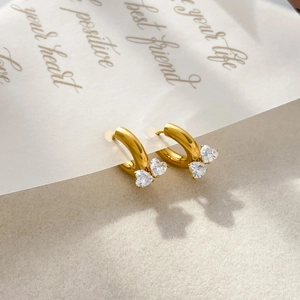 Close-up of golden small hoop earrings featuring two heart-shaped clear cubic zirconia