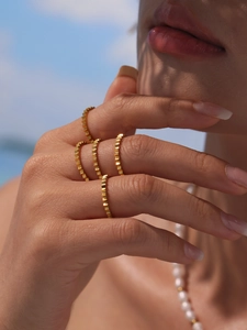 Detail of four gold gear-textured stainless steel rings stacked on model's hand