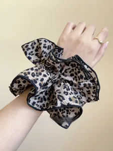 Dettaglio di un grande elastico scrunchie leopardato con bordo nero indossato al polso