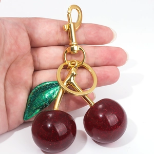 Detailed view of cherry keychain with dark red glitter fruit and green leaves on gold hook