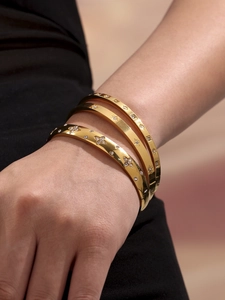 Detailed view of three stackable gold bangles with clover, star, and zircon inlay on wrist