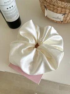 Detailed view of oversized cream satin scrunchie with rich folds and silk texture