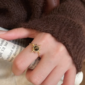 Detailed close-up of a golden sun-shaped ring featuring a brown tiger eye bead on finger