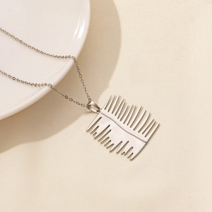 Macro shot of silver stainless steel leaf pendant on white textured paper with sharp shadows