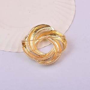 Elegant gold abstract swirl brooch with textured layers displayed on a white shell prop