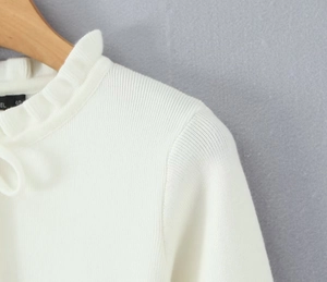 Dettaglio del cardigan in maglia bianca con scollo a balze e trama a coste fini