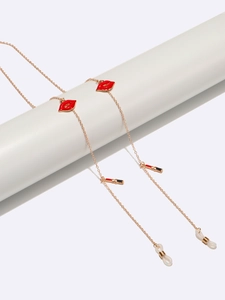 Golden metal eyewear chain with red lip and lipstick charms on a white display