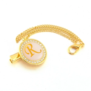 Detail of golden pacifier clip with rhinestone initial R and elegant double link chain