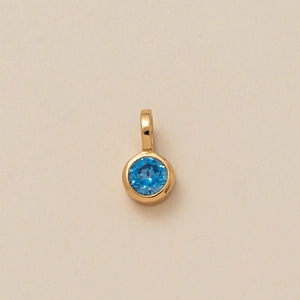 Close-up of golden circular pendant with a round faceted blue gemstone in bezel setting