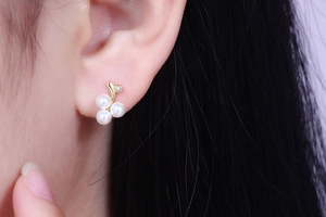 Macro view of gold pearl stud earrings featuring three white pearls and sparkling diamond