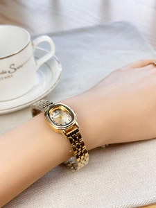 Elegant gold oval quartz watch with metal mesh band worn during a tea party session