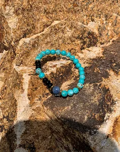 Macro detail of turquoise and black onyx beaded bracelet with gold spacers on rock
