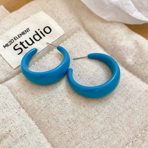 Detail view of glossy bright blue C-shaped acrylic hoop earrings on a textured fabric pouch