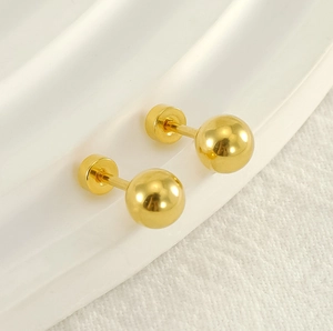 Close-up of golden ball stud earrings with polished steel texture and screw back detail